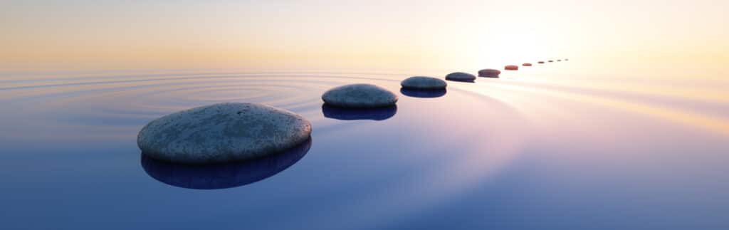 Chemin de galets zen sur l'eau calme, reflets doux et ciel apaisant à l'aube. Symbole de sérénité et progression.