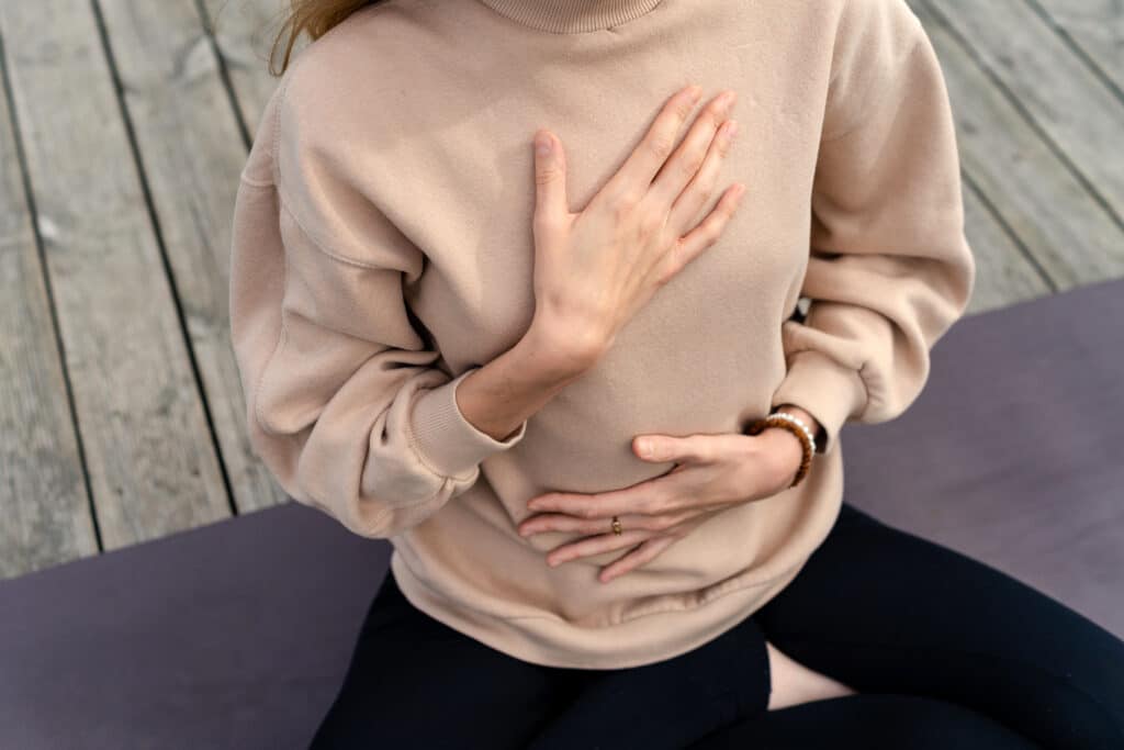 Méditation et Respiration Consciente: Bien-être et Calme Femme assise en tailleur sur un tapis de yoga, mains sur le cœur et le ventre pour la méditation et la respiration consciente.