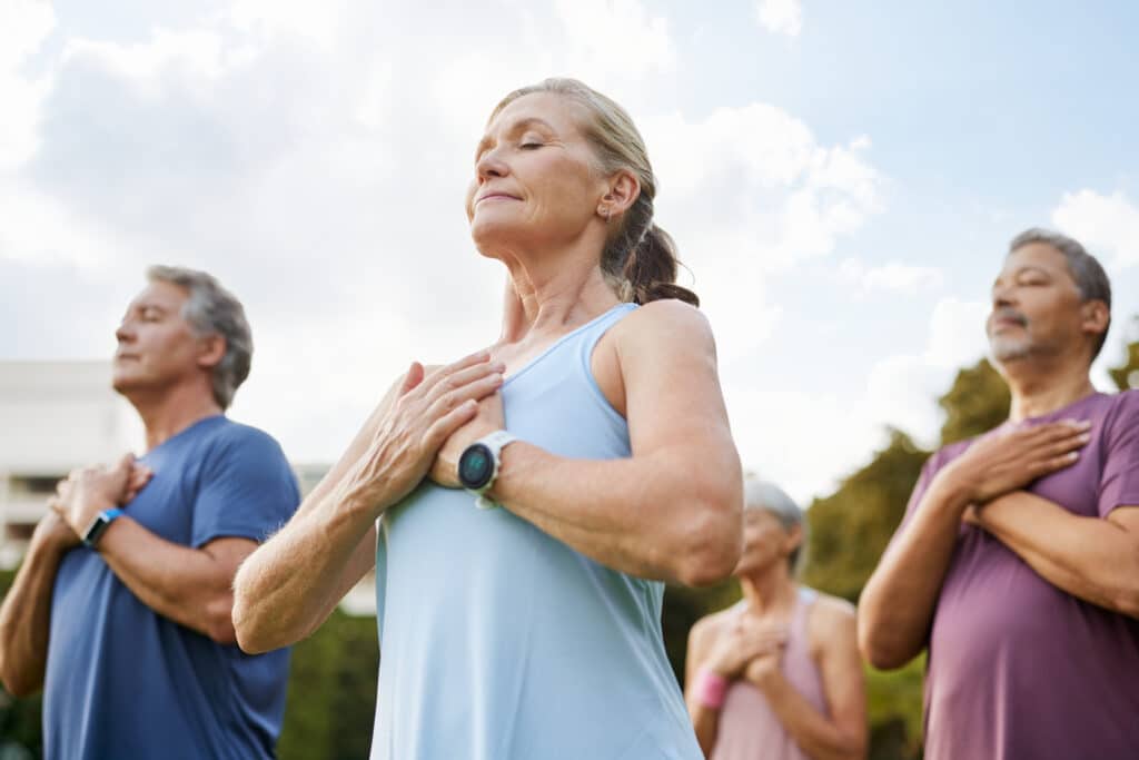 Seniors en méditation : bien-être et sérénité en plein air. Seniors en méditation en plein air, yeux fermés et mains sur le cœur. Calme et bien-être pour un groupe d'adultes.